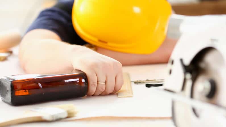 sleeping drunk worker in yellow helmet holding the bottle